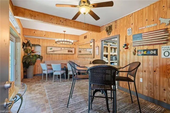 Dining space with ceiling fan with notable chandelier and wood walls