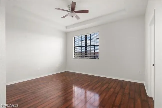 Empty room with a raised ceiling, dark wood-style floors, and ceiling fan