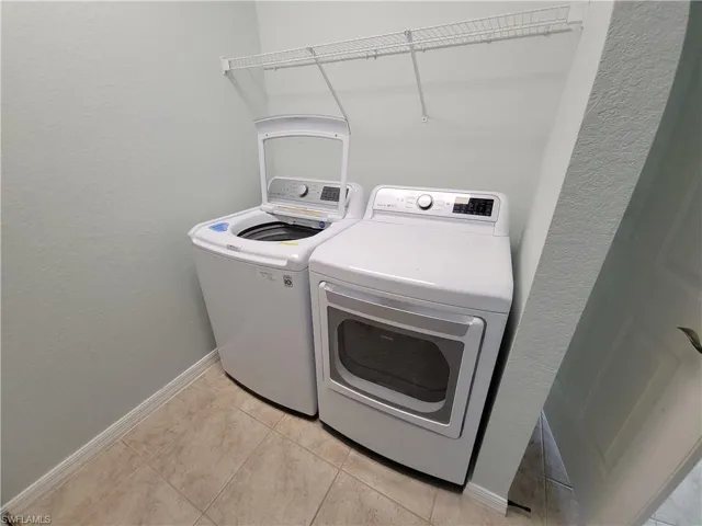 Washroom featuring a textured wall, independent washer and dryer, and light tile patterned flooring