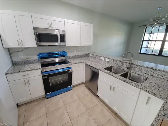 Kitchen with appliances with stainless steel finishes, white cabinets, light stone countertops, and light tile patterned floors