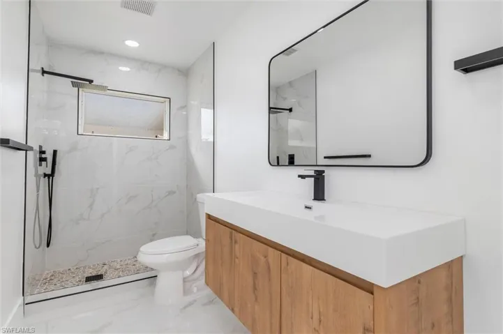 Bathroom featuring vanity, toilet, and a tile shower