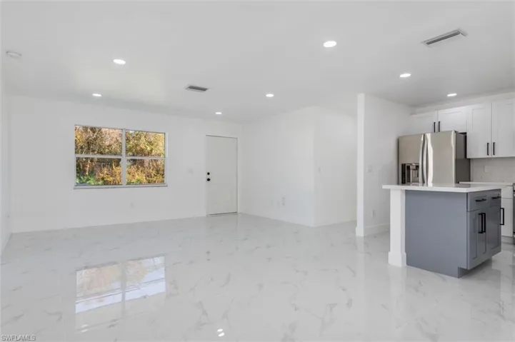 Kitchen featuring white cabinetry, gray cabinetry, a center island, and stainless steel fridge with ice dispenser