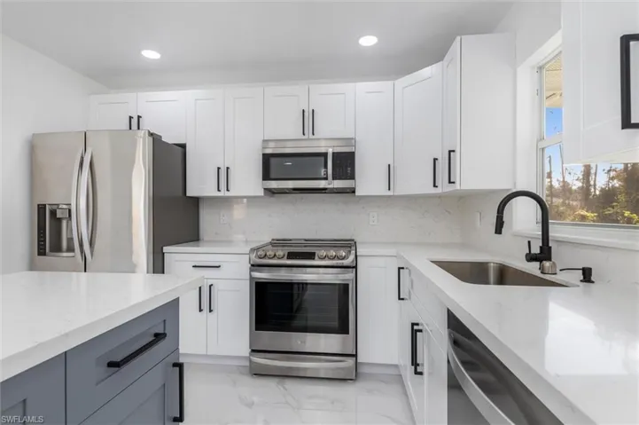 Kitchen with light stone countertops, sink, white cabinets, and stainless steel appliances