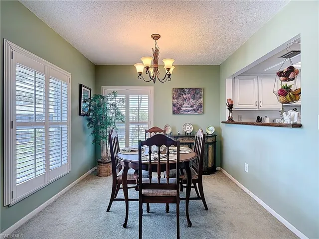 Dining space with a textured ceiling, light colored carpet, and a chandelier