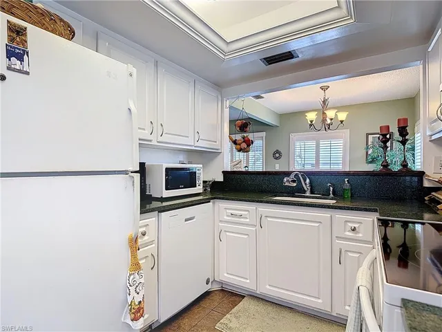 Kitchen featuring white appliances, white cabinets, a chandelier, dark tile patterned flooring, and dark stone counters