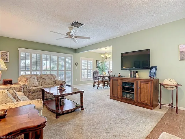 Living room with a textured ceiling, ceiling fan, light carpet, a chandelier, and light tile patterned flooring
