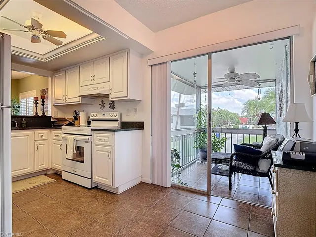 Kitchen with ceiling fan, white appliances, white cabinets, dark tile patterned flooring, and a textured ceiling
