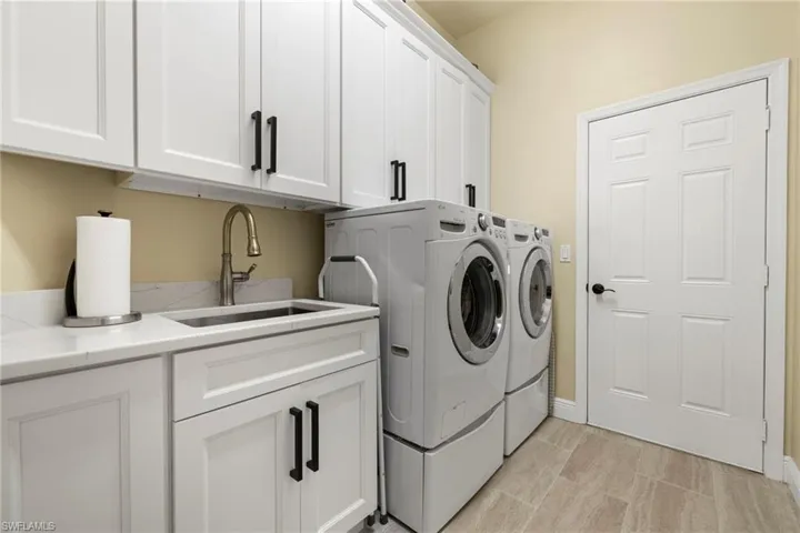 Renovated laundry with Sink, cabinetry, washer, dryer. Located convenient to kitchen and garage entry.