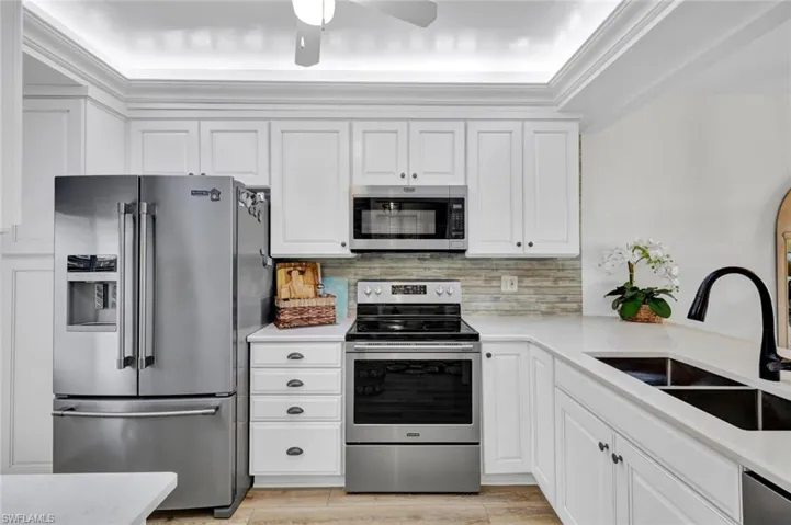 Kitchen with stainless steel appliances, light stone countertops, white cabinetry, and ornamental molding