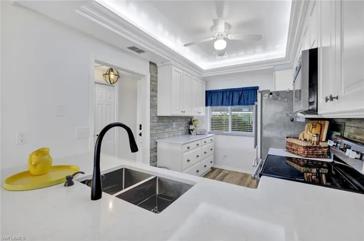 Kitchen featuring white cabinets, stainless steel appliances, backsplash, a raised ceiling, and ceiling fan