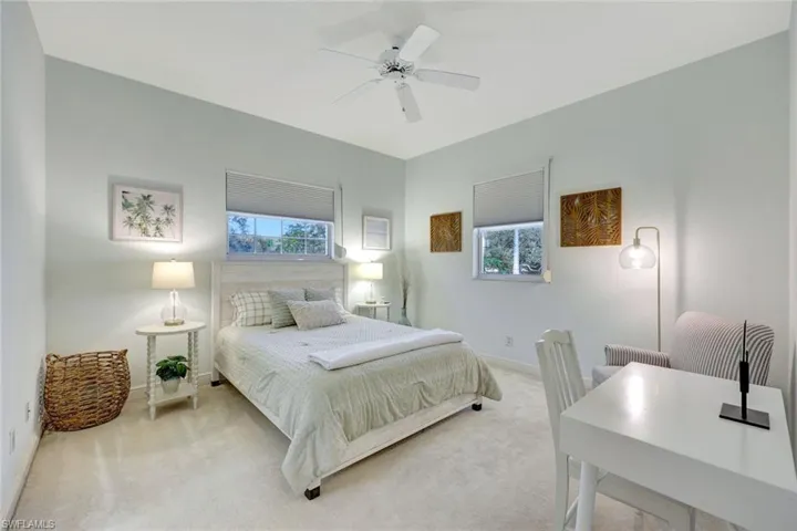 Carpeted bedroom with multiple windows, a ceiling fan, and an office area