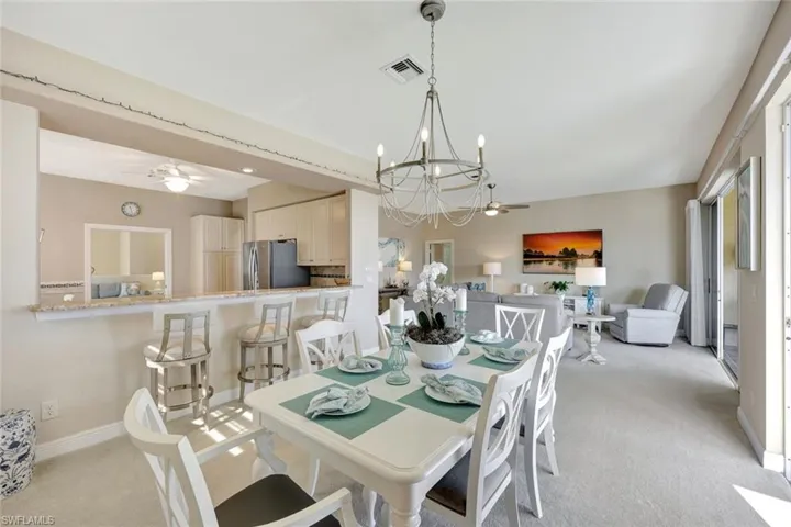 Dining area with a ceiling fan, light colored carpet, and a chandelier