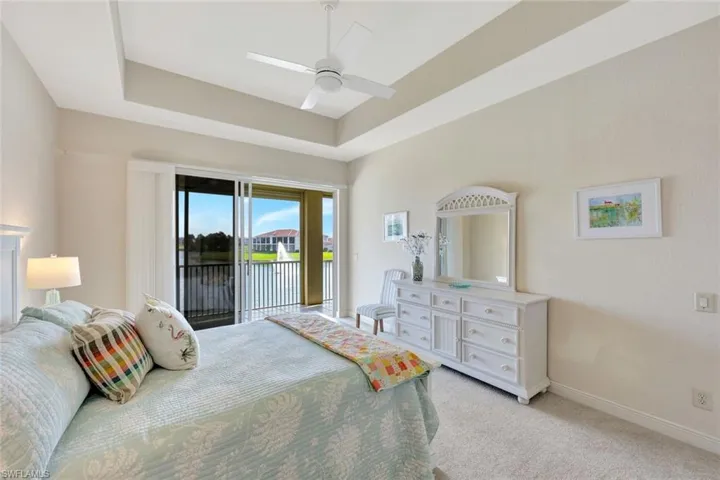 Bedroom with a raised ceiling, a water view, light colored carpet, access to exterior, and ceiling fan