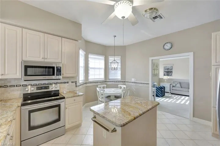 Kitchen featuring appliances with stainless steel finishes, a center island, light stone counters, light tile patterned floors, and pendant lighting
