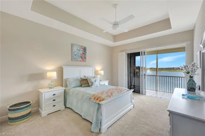 Bedroom with a raised ceiling, a water view, access to outside, ceiling fan, and light colored carpet