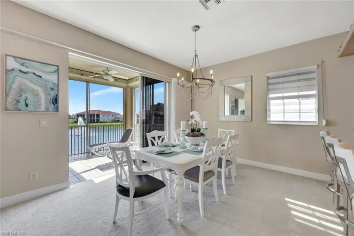 Dining room featuring a water view, light colored carpet, a chandelier, and a ceiling fan