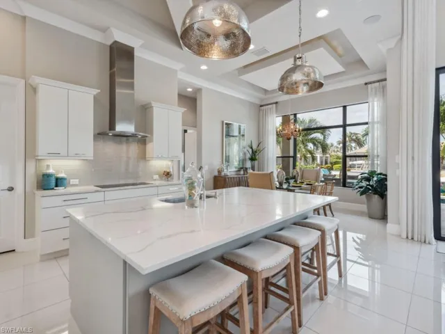Kitchen featuring pendant lighting, a kitchen island with sink, white cabinets, wall chimney exhaust hood, and black electric cooktop