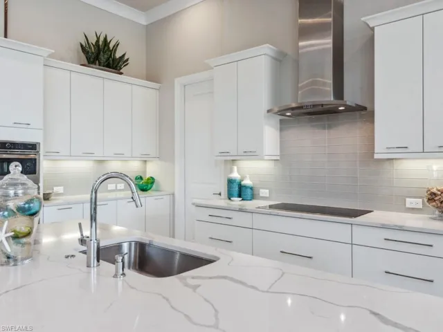 Kitchen with light stone countertops, stainless steel oven, white cabinets, and wall chimney range hood