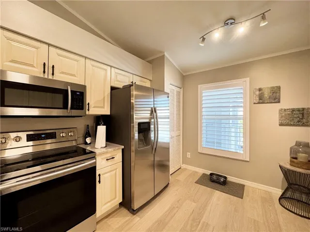 Kitchen featuring stainless steel appliances, crown molding, light wood-type flooring, and white cabinets