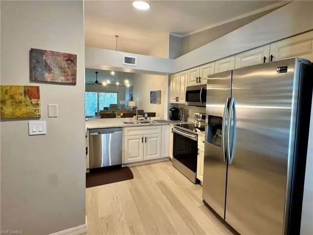 Kitchen with stainless steel appliances, decorative light fixtures, white cabinets, light wood-style flooring, and light stone countertops