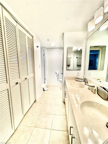 Bathroom featuring a closet, double vanity, light tile patterned floors, and a textured ceiling