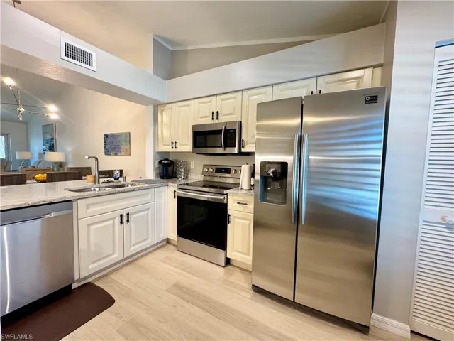 Kitchen with stainless steel appliances, light stone counters, light wood-style flooring, open floor plan, and white cabinetry