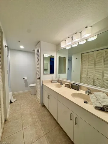 Full Master bathroom featuring a closet, double vanity, a textured ceiling, and light tile patterned floors
