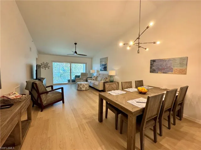 Dining space with light wood finished floors, vaulted ceiling, a ceiling fan, and a chandelier