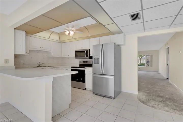 Kitchen featuring appliances with stainless steel finishes, light countertops, tasteful backsplash, white cabinetry, and a drop ceiling