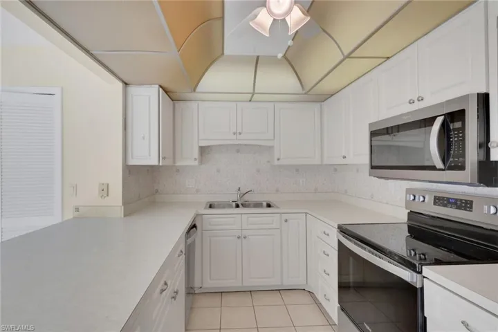 Kitchen with stainless steel appliances, light tile patterned floors, light countertops, backsplash, and white cabinetry