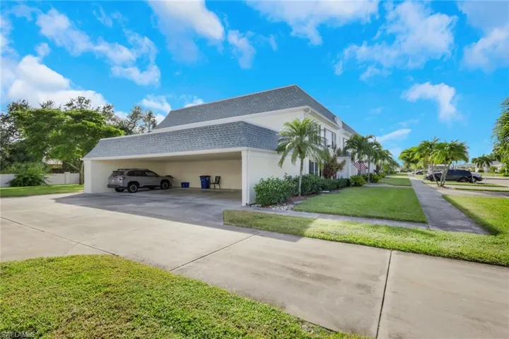 View of side of property featuring driveway, a carport, roof with shingles, a lawn, and stucco siding