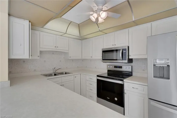 Kitchen featuring stainless steel appliances, light countertops, decorative backsplash, and white cabinets