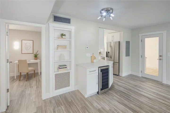 Kitchen featuring beverage cooler, light countertops, light wood-type flooring, stainless steel fridge with ice dispenser, and white cabinets