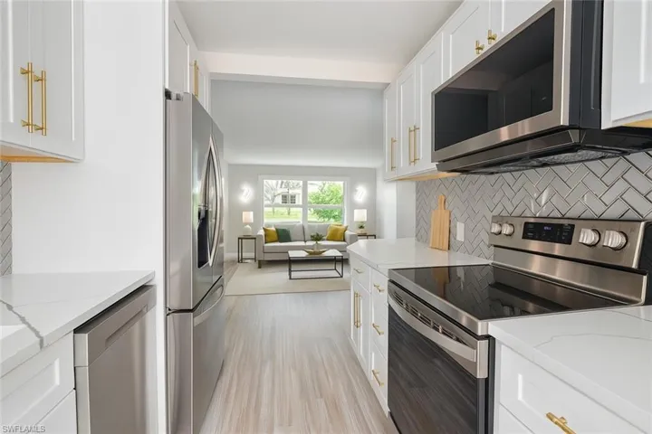 Kitchen featuring appliances with stainless steel finishes, tasteful backsplash, white cabinets, light wood-type flooring, and light stone countertops