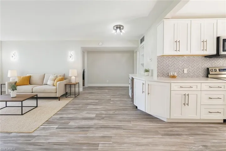 Kitchen featuring stainless steel appliances, decorative backsplash, white cabinetry, light countertops, and light wood finished floors