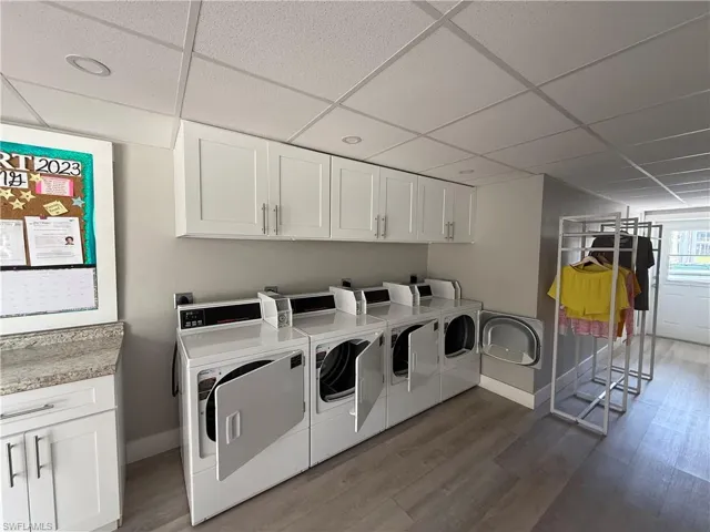 Clothes washing area with washing machine and clothes dryer, cabinet space, dark wood finished floors, and baseboards