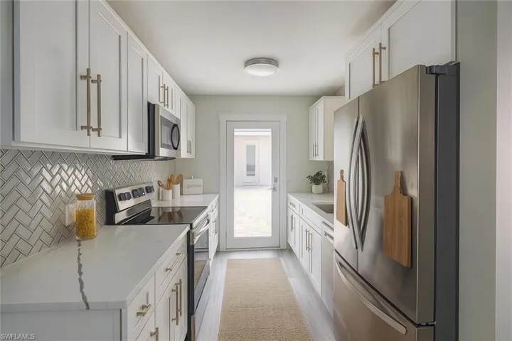 Kitchen featuring appliances with stainless steel finishes, white cabinetry, light stone counters, backsplash, and light wood finished floors