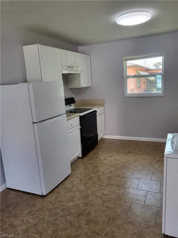 Kitchen with freestanding refrigerator, white cabinetry, range with electric cooktop, and light countertops