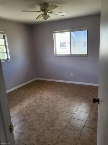 Empty room with a ceiling fan, plenty of natural light, and tile patterned flooring
