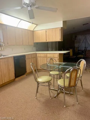 Kitchen with black dishwasher, sink, light brown cabinets, light carpet, and ceiling fan