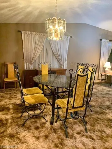 Carpeted dining room with a chandelier and vaulted ceiling
