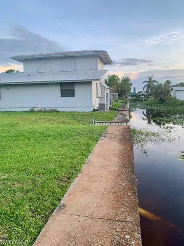 Property exterior at dusk featuring cooling unit, a water view, and a lawn