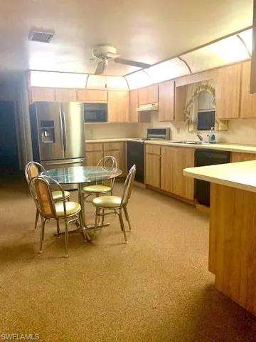 Kitchen with light brown cabinetry, sink, black appliances, and ceiling fan