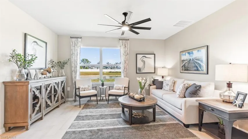 Model Home. The living area features light-toned walls, a ceiling fan, and large windows providing views of the outdoors