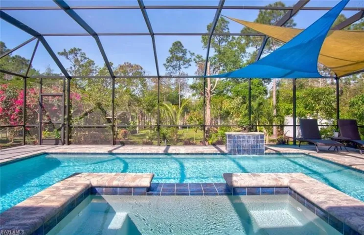 Screened enclosure featuring a swimming pool, integrated spa, and a tiled water feature