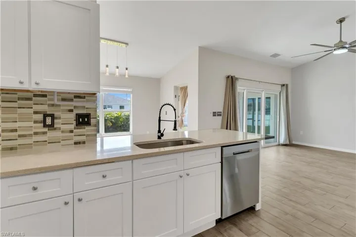 Kitchen with light hardwood / wood-style floors, sink, white cabinetry, light stone countertops, and stainless steel dishwasher
