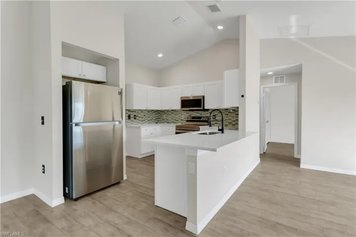 Kitchen with appliances with stainless steel finishes, white cabinetry, high vaulted ceiling, light wood-type flooring, and sink