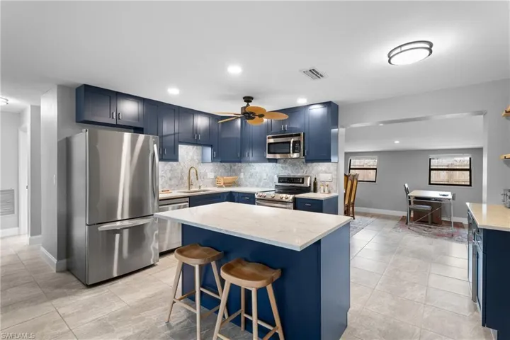 Kitchen with appliances with stainless steel finishes, sink, blue cabinets, decorative backsplash, and a breakfast bar