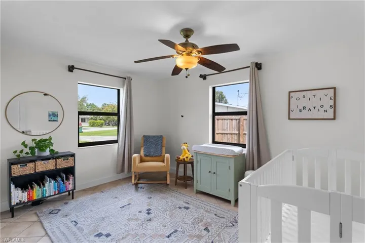 Bedroom with multiple windows, a nursery area, light tile patterned floors, and ceiling fan