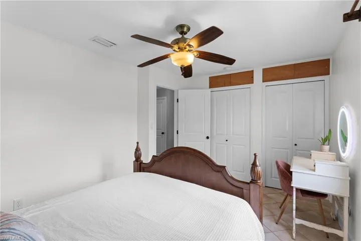 Bedroom with multiple closets, light tile patterned floors, and ceiling fan